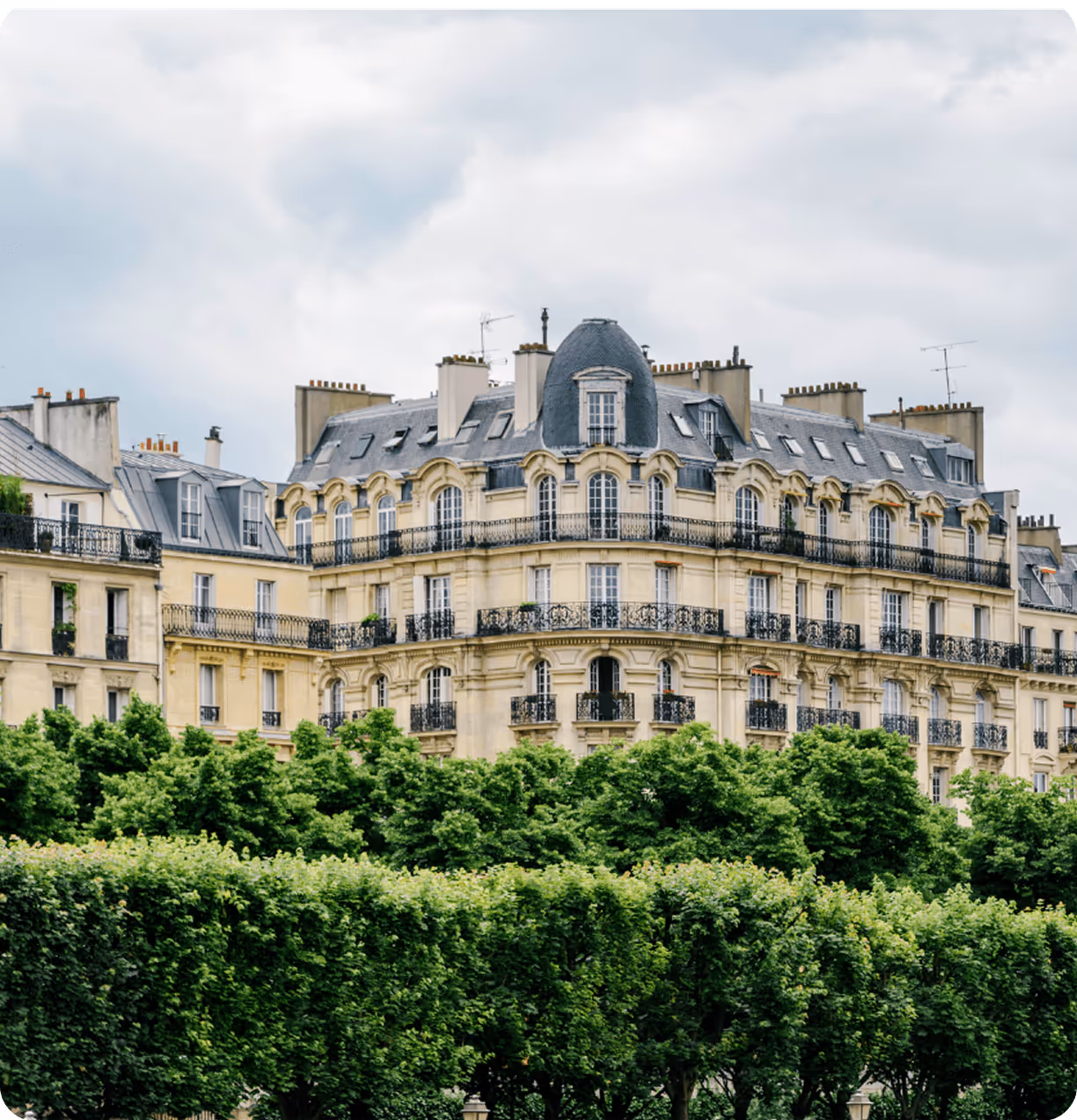 Un immeuble haussmannien derrière une haie d'arbres à Paris