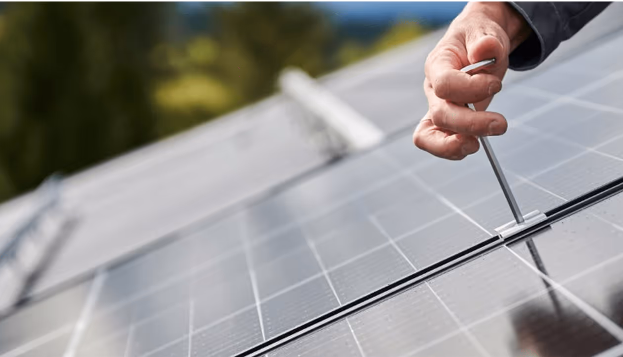 Hand justiert Solarmodul mit Schraubendreher, nachhaltige Energieinstallation im Freien.