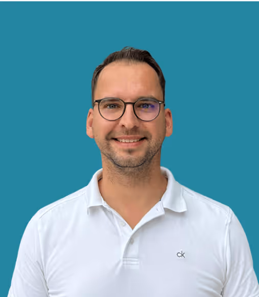 Mann mit Brille in weißem Polohemd lächelt vor blauem Hintergrund.