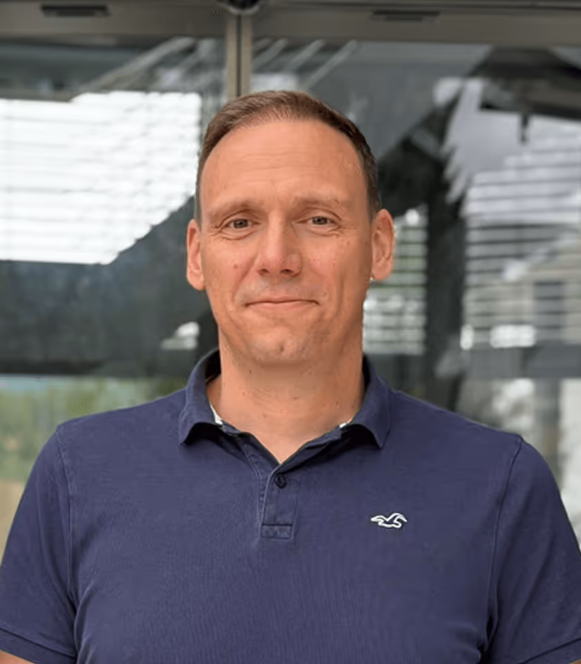 Lächelnder Mann in blauem Polohemd vor modernem Gebäude mit Glasfassade.