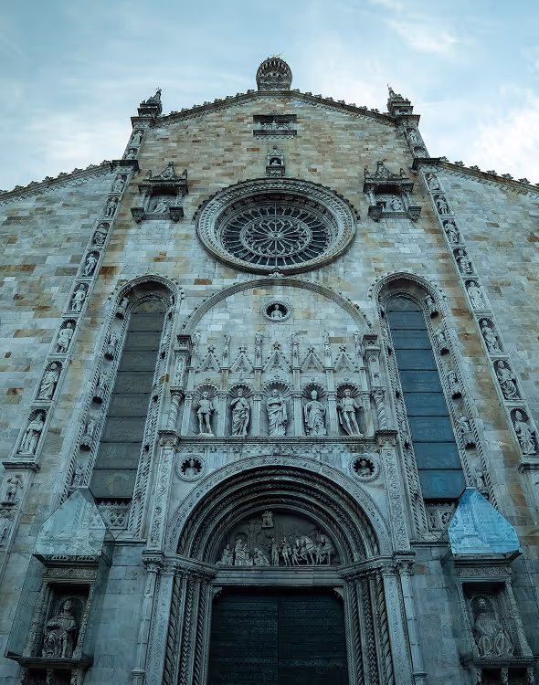 Фасад исторической церкви с детальной резьбой по камню, статуями и большим круглым витражным окном.