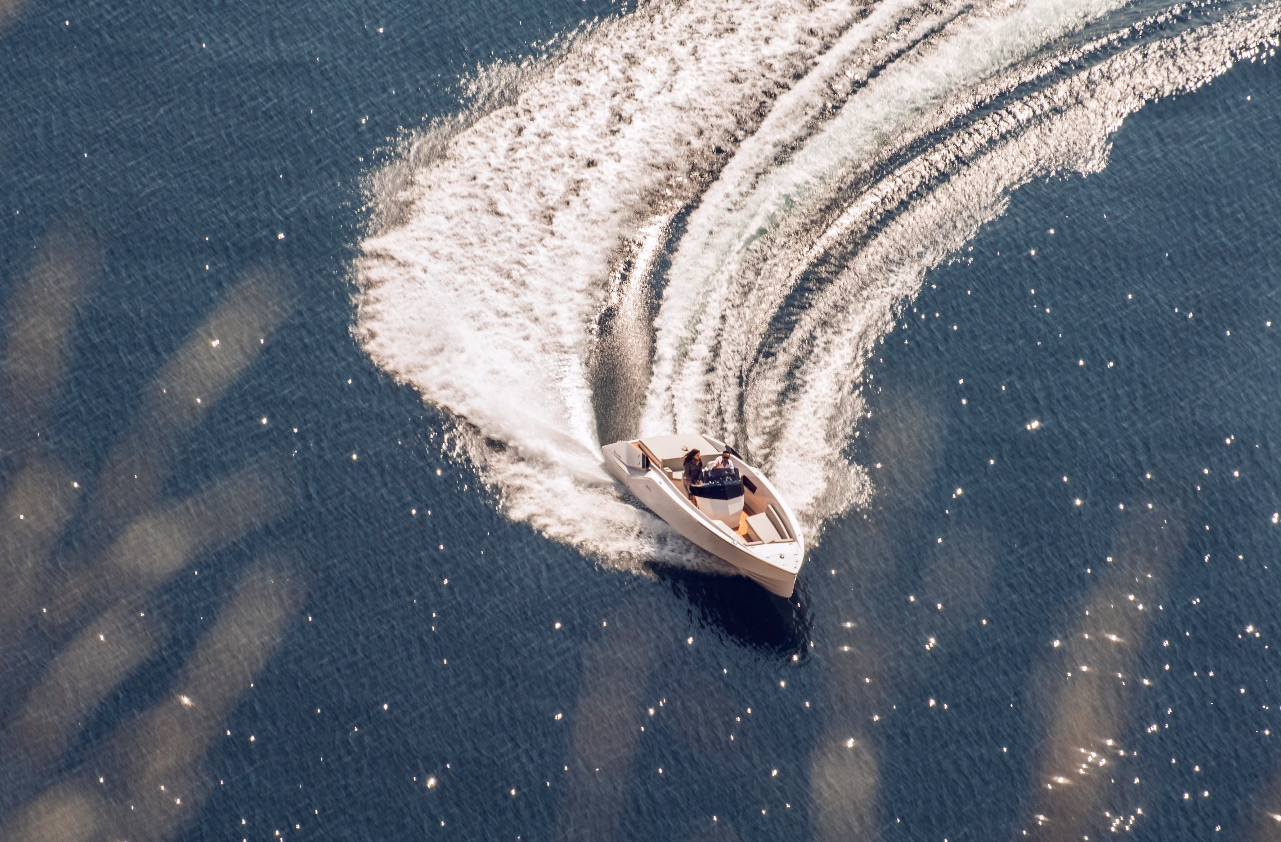 White motorboat with two people turning sharply on sparkling blue water, leaving a curved wake.