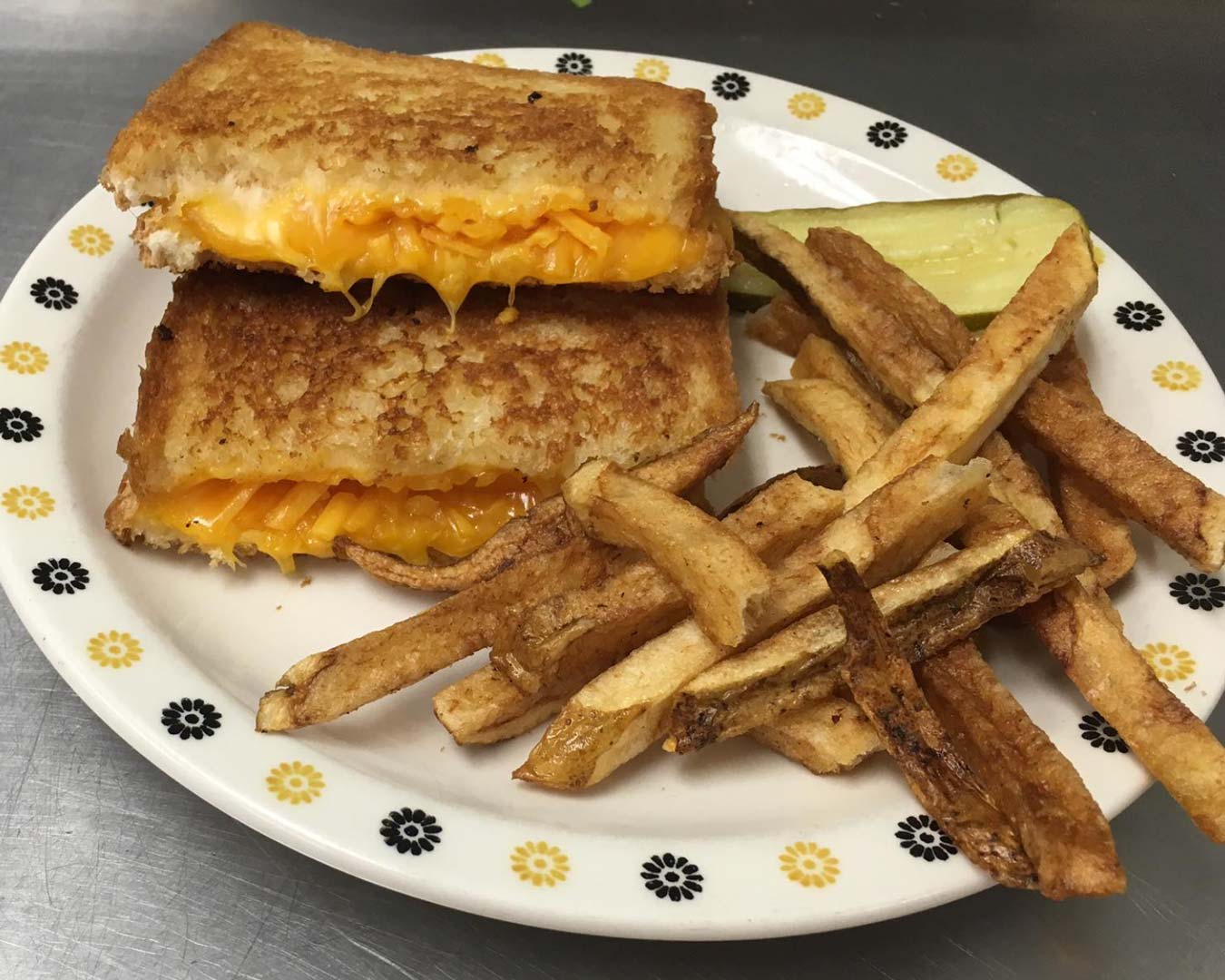 A grilled cheese sandwich with melted cheese and crispy edges, served alongside golden French fries on a white plate.