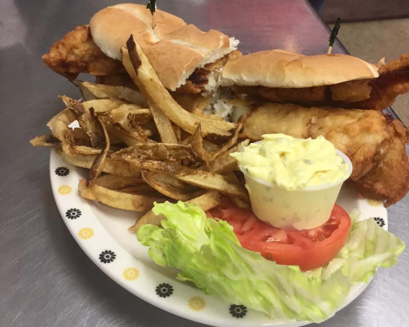 A plate of fish sandwich and chips featuring crispy fried fish, golden fries, and a slice of tomato.