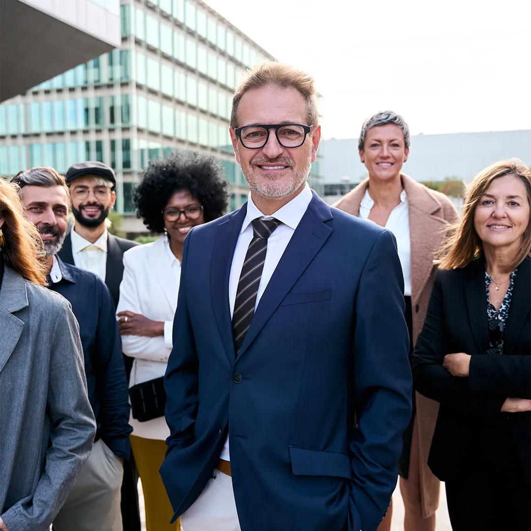 Gruppo di sei professionisti sorridenti in abbigliamento formale in un contesto urbano moderno.