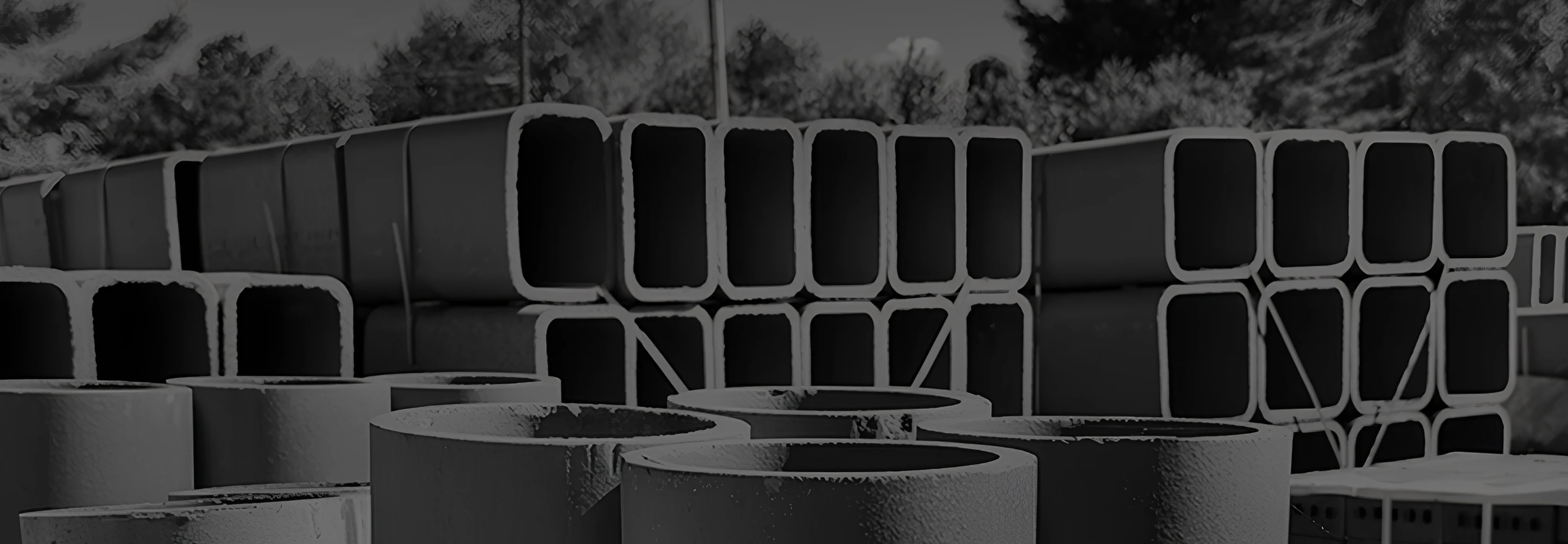 Stacks of large concrete pipes and rectangular hollow sections stored outdoors.