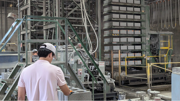 Worker in a white shirt and cap operating machinery inside an industrial factory.