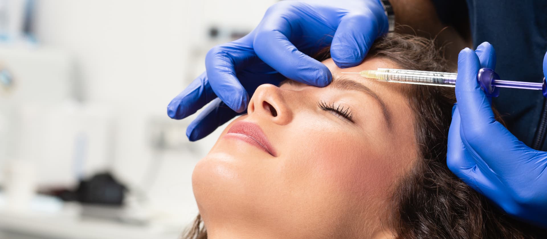 Close-up of a woman receiving a cosmetic injection in her forehead from a professional wearing blue gloves.