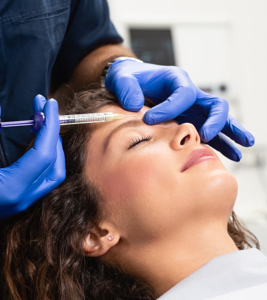 Woman receiving a cosmetic injection in her forehead from a healthcare professional wearing blue gloves.
