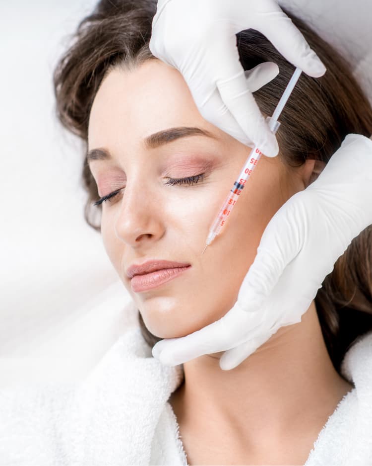 Gloved hands injecting a cosmetic filler into a woman's cheek during a beauty treatment.