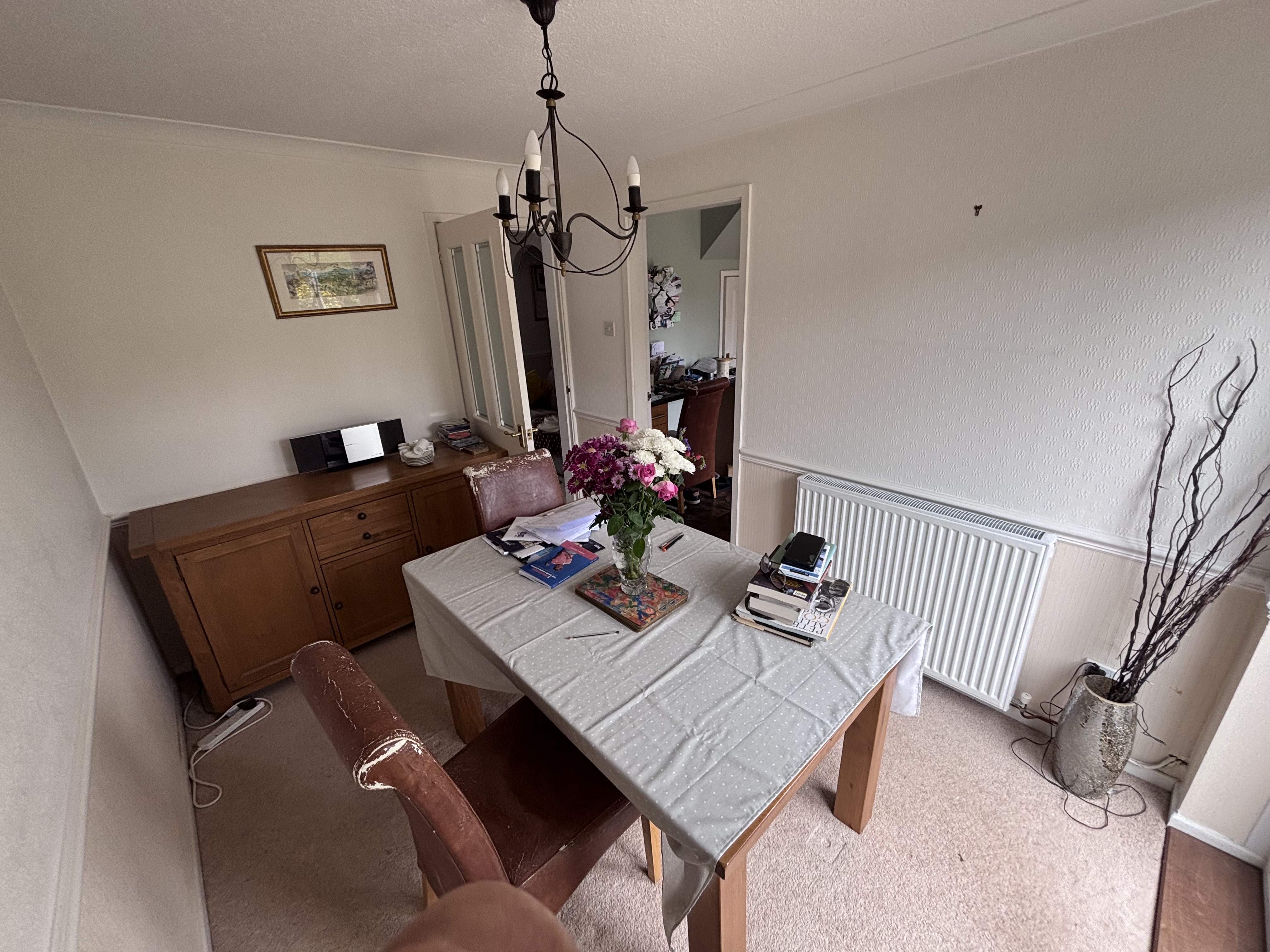 Outdated dining room with wooden furniture, carpet flooring, and wallpaper before renovation.