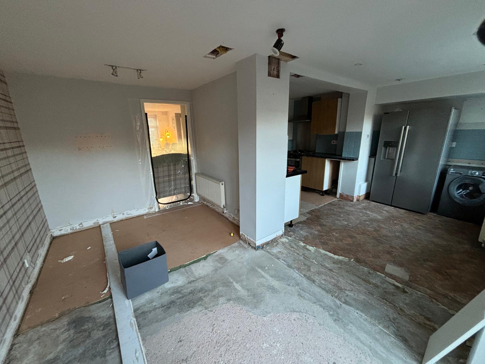 Kitchen renovation in progress with stripped flooring, exposed walls, and partially removed units.