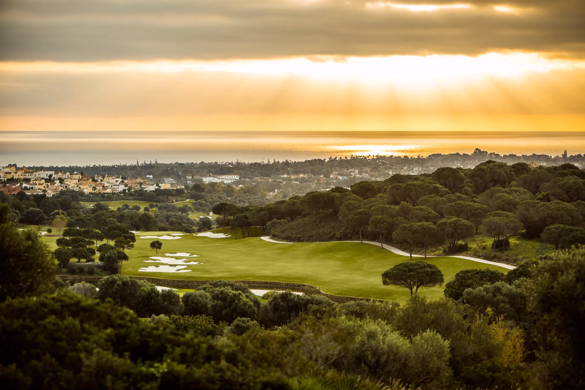 La Reserva Golf course with bunkers and trees at sunset with Sotogrande and the ocean in the background.