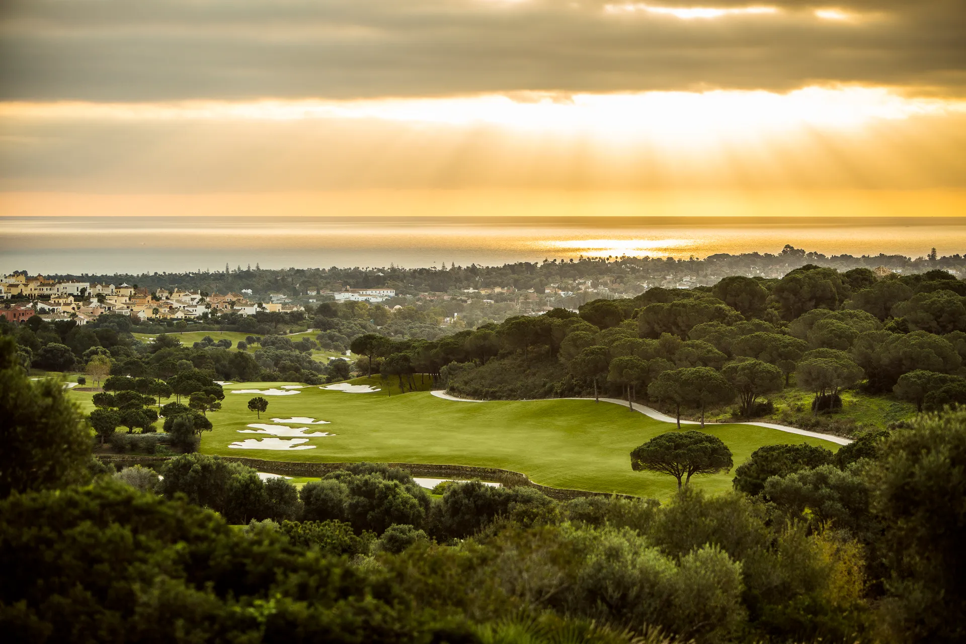 La Reserva Golf course with bunkers and trees at sunset with Sotogrande and the ocean in the background.