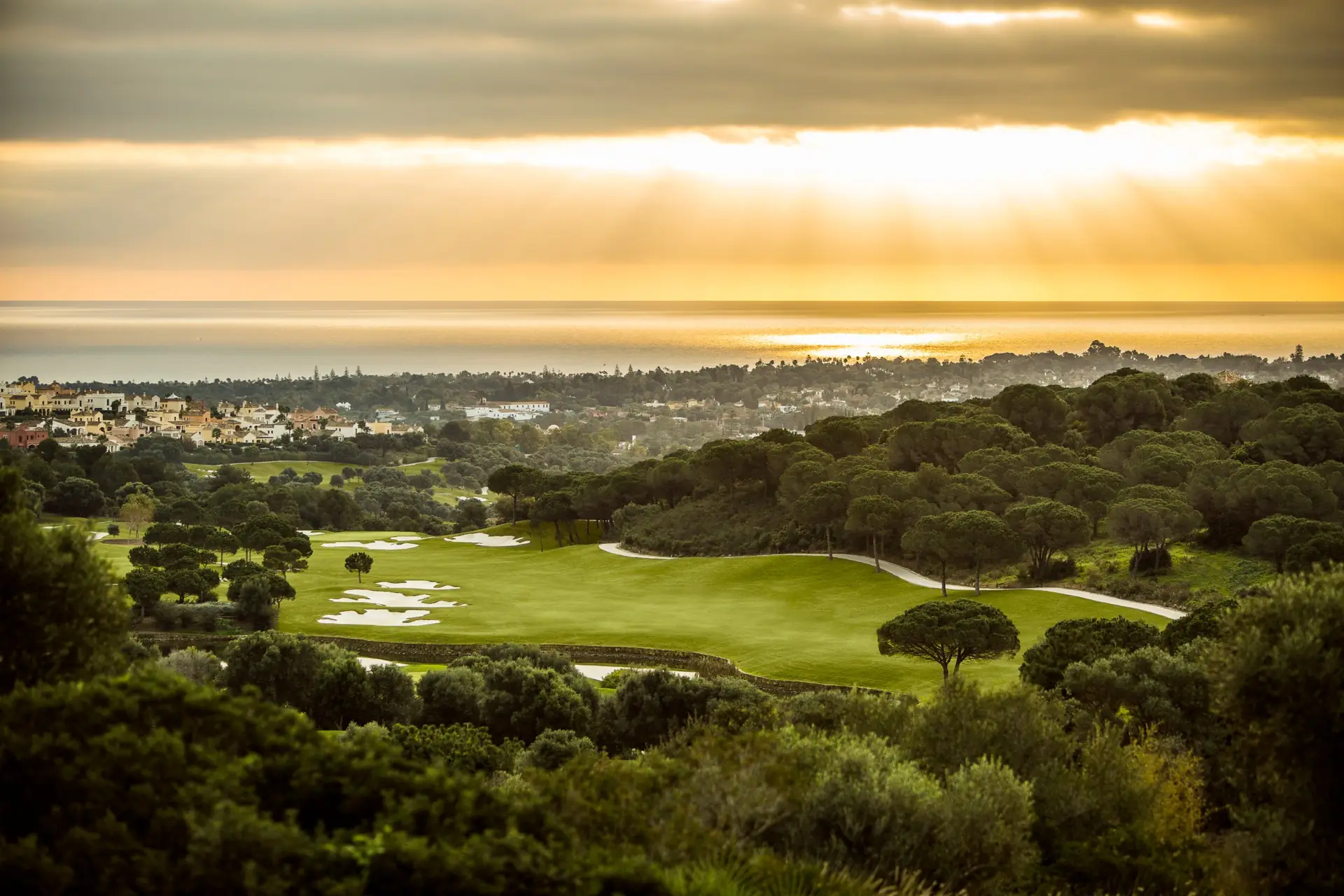 La Reserva golf course with bunkers and trees at sunset, with Sotogrande and the sea in the background