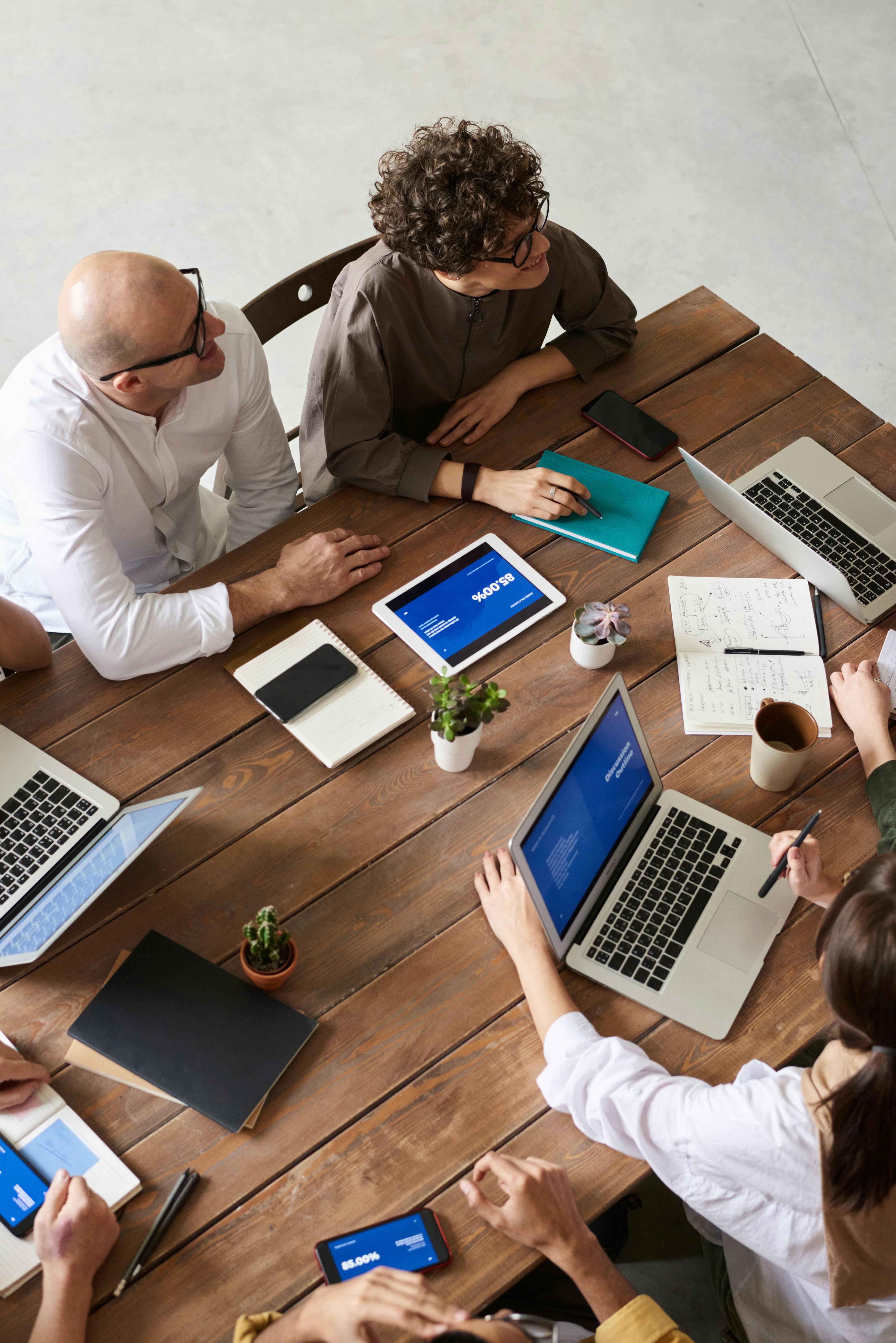 Overhead picture of man, woman and others in a business meeting with notepads, tablets and computers on a wooden conference table