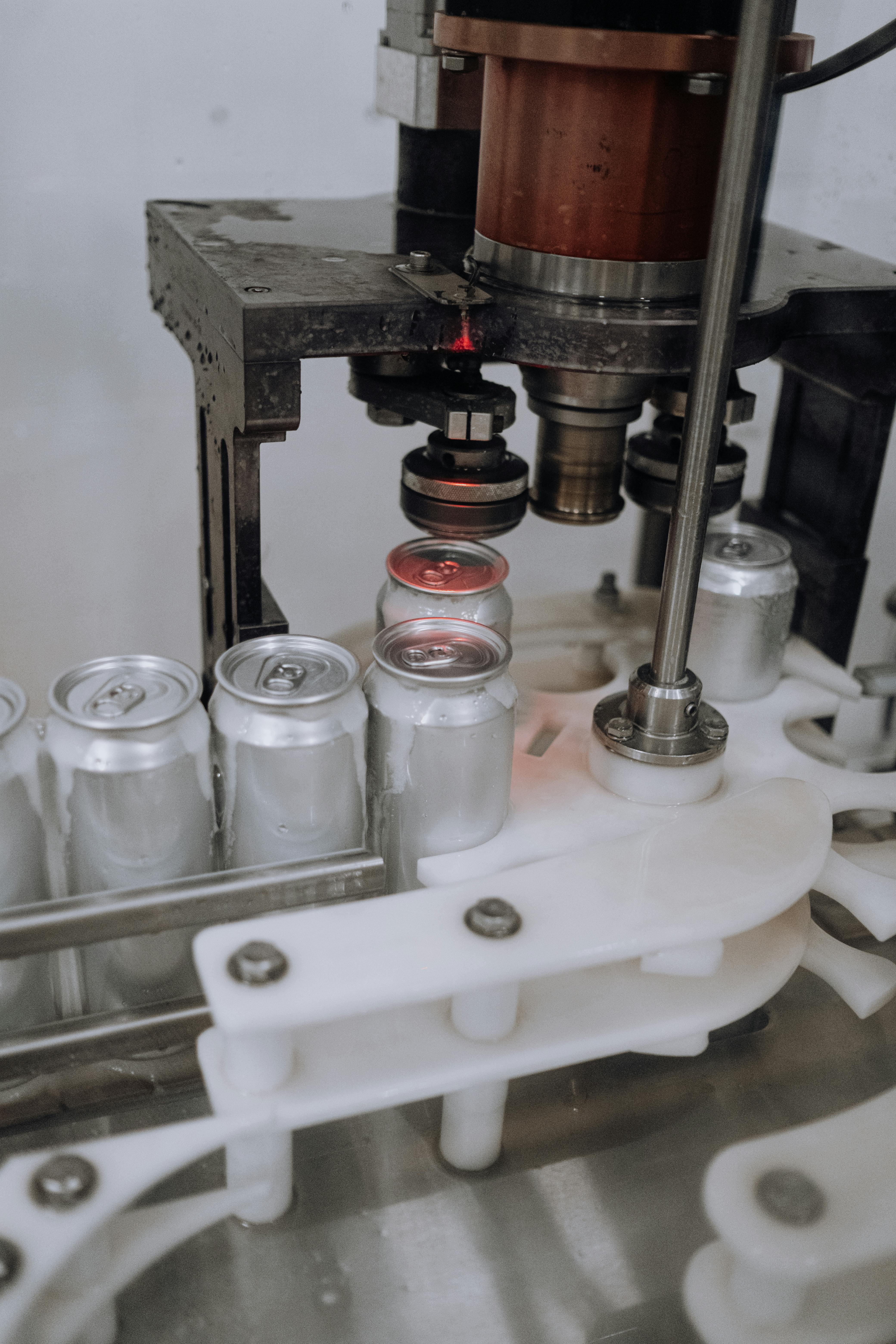 A picture of an assebly line, where unlabeled cans are going throuhg a machine that seals the top on