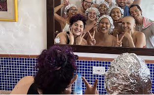 Group of seven people smiling and making peace signs in a mirror selfie, with two people facing the mirror.
