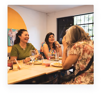 Four women sitting at a table in a cozy café, enjoying drinks and food while engaged in lively conversation.