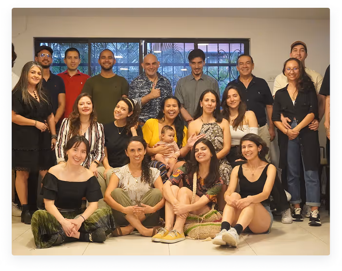 Group photo of twenty people including men, women, and a baby, posing indoors in front of a window.