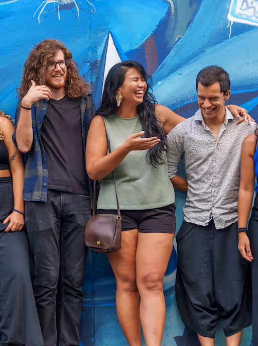 Three friends standing closely and laughing in front of a blue graffiti wall.
