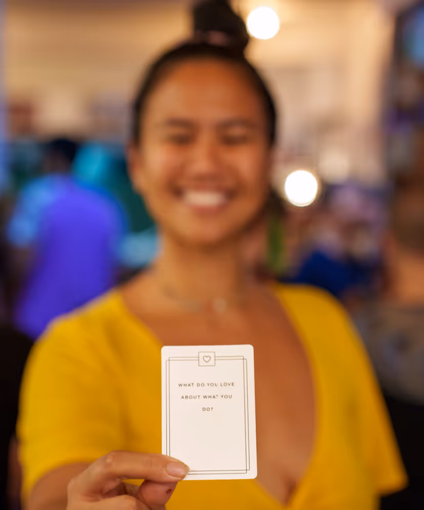 Person in yellow top smiling and holding a card that reads 'What do you love about what you do?'