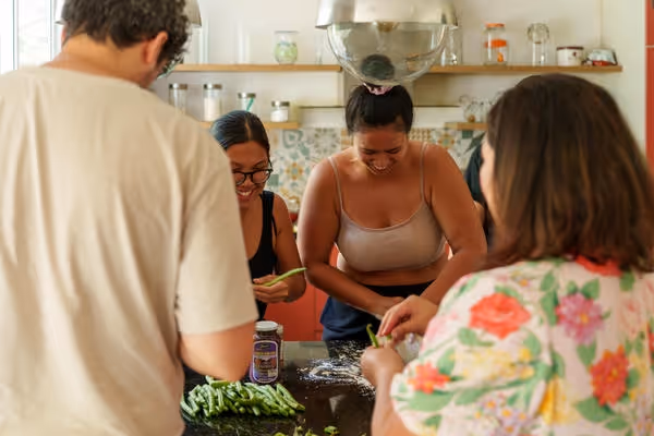 Four people gathered around a kitchen counter preparing green beans together, smiling and engaged in cooking.