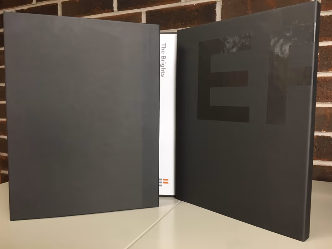 Two dark gray binders standing open on a desk with a smaller white book titled The Brights between them.