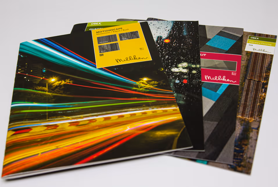 Stack of colorful Milliken brochures with motion blur and geometric designs on white surface.
