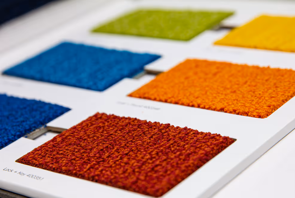Samples of carpet swatches in various colors including red, orange, blue, yellow, and green on a white board.