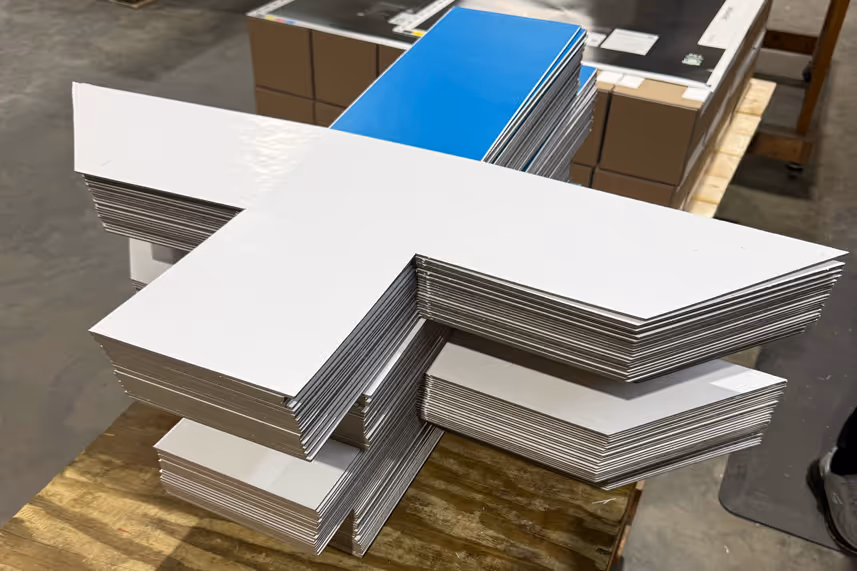 Stacks of white and blue cardboard cutouts shaped for custom box assembly on a wooden pallet.