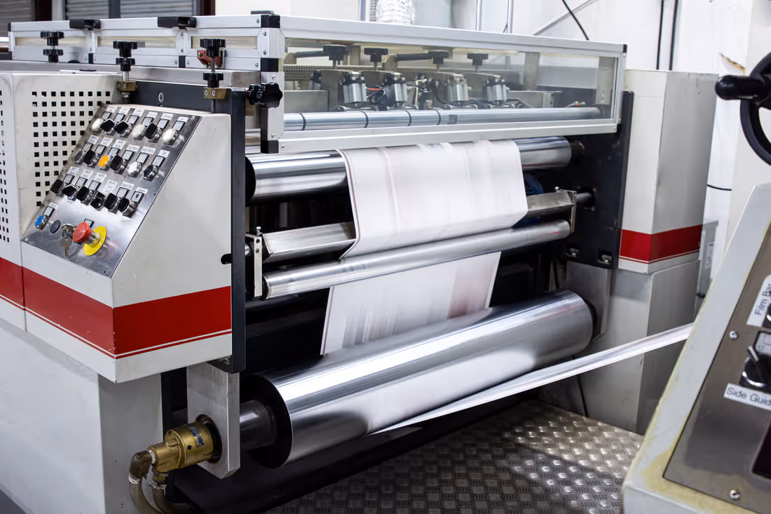 Industrial laminator machine with metal rollers laminating a sheet of paper in a factory setting.