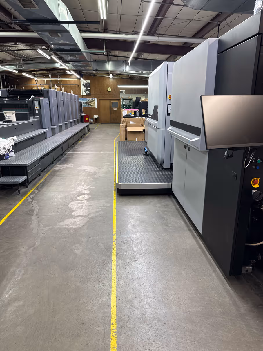Interior of a printing facility with large offset and digital printing machines along the aisle.