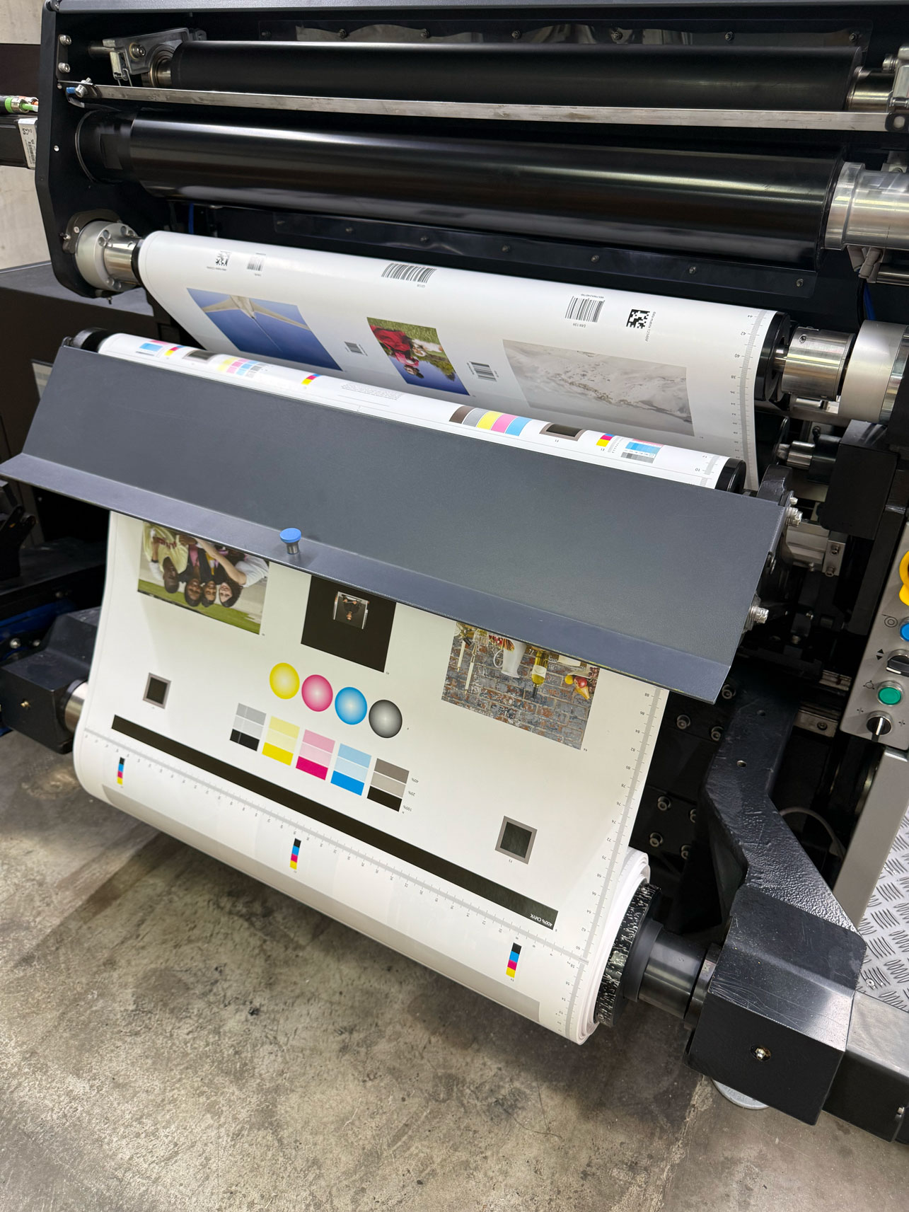 Roll-to-roll digital printing press with partially printed paper featuring test images and color swatches.