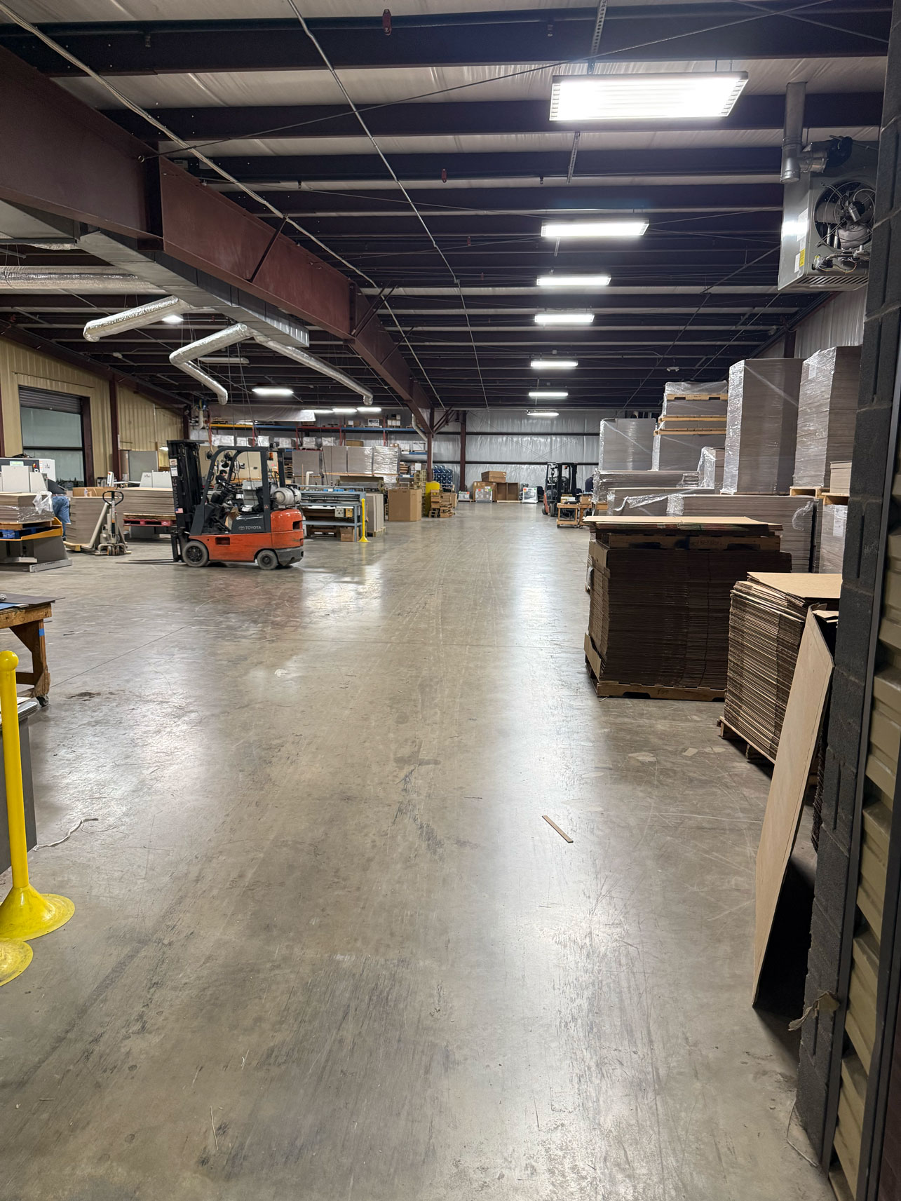 Spacious warehouse interior with stacked pallets, forklift, and industrial lighting overhead.