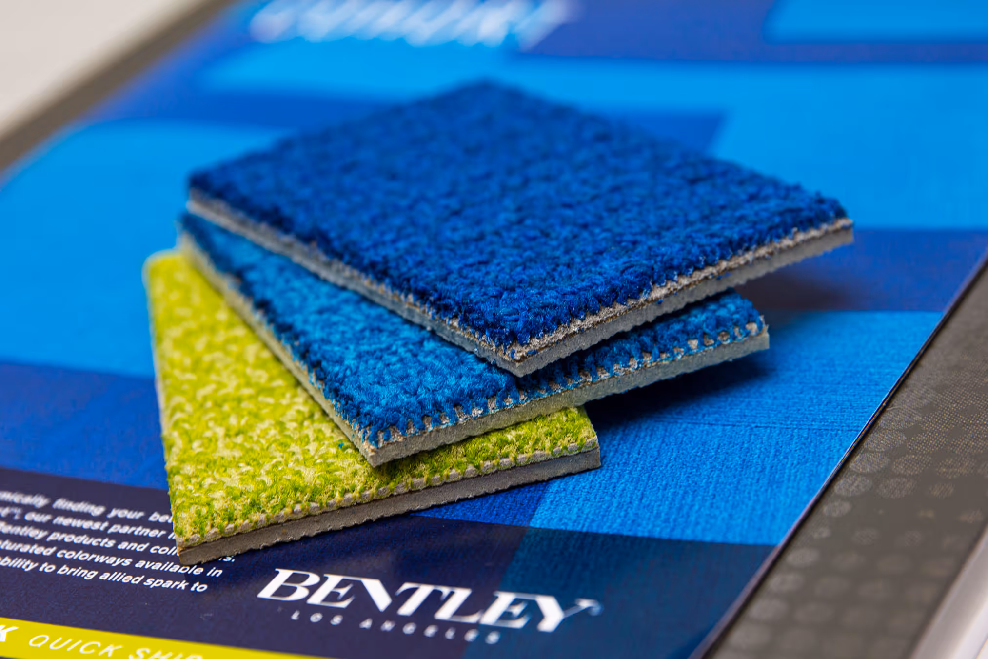 Three fabric swatches in green, light blue, and dark blue stacked on a Bentley brochure.