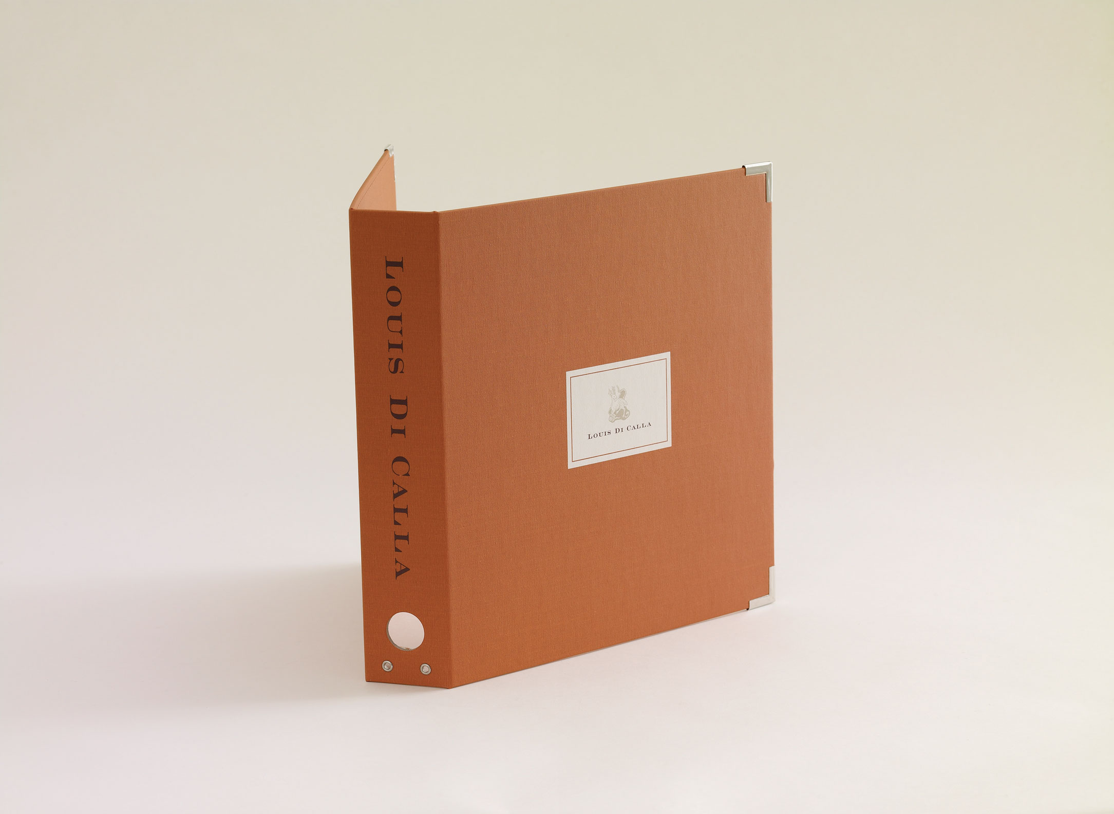 Orange square binder labeled 'Louis Di Calla' standing upright on a light background.