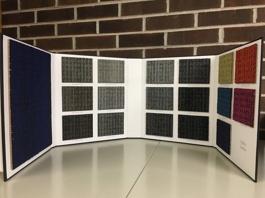 Open carpet sample book displaying various textured fabric swatches in neutral and bright colors.