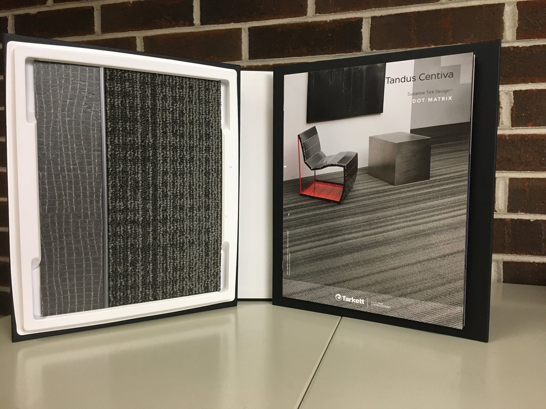 Open carpet sample booklet showing textured carpet swatches and a modern chair on striped flooring.
