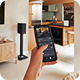 Hand holding a smartphone controlling a smart home device in a modern living room and kitchen.