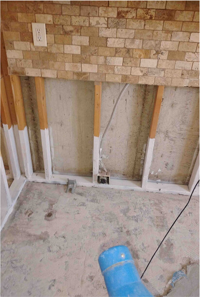 Lower drywall removed below a stone tile wall with an air mover drying the room