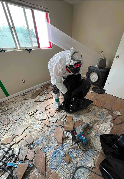 Technician in protective gear removing damaged floor tile inside containment