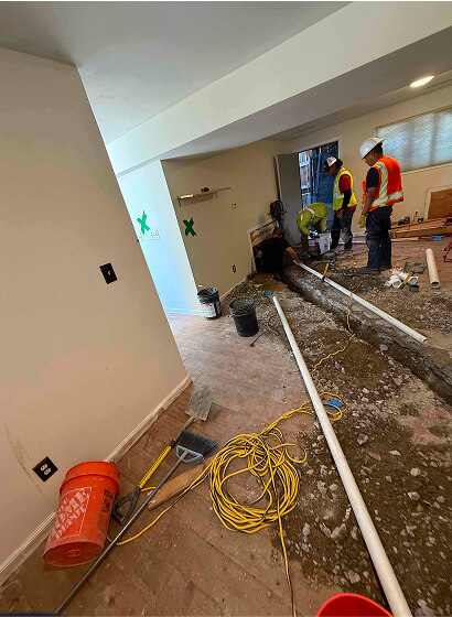 Crew replacing under-floor plumbing in a trench during home restoration