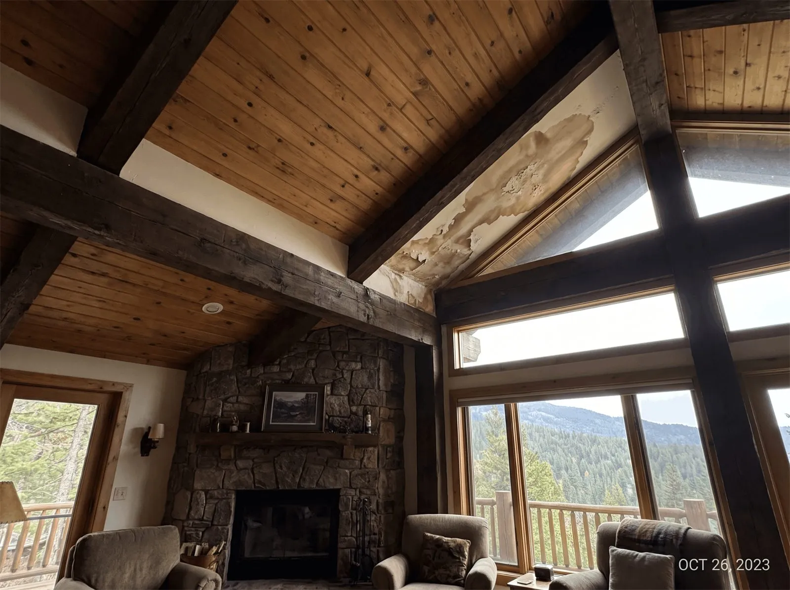 Water stain spreading across a vaulted wood ceiling above the windows of a mountain living room