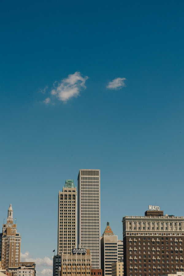 Downtown Tulsa skyline with various high-rise buildings under a clear blue sky with two small clouds.