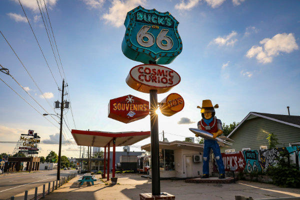 Vintage road sign for Buck's on Route 66 with Cosmic Curios, souvenirs, and toys, next to a large cowboy statue holding a rocket.