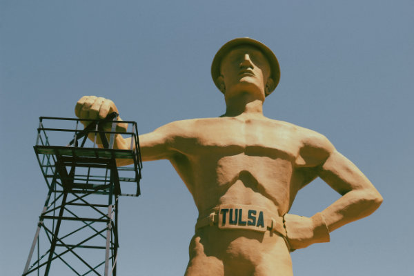 The Golden Driller statue in Tulsa, Oklahoma, standing tall with a hard hat and holding a metal structure with one hand.