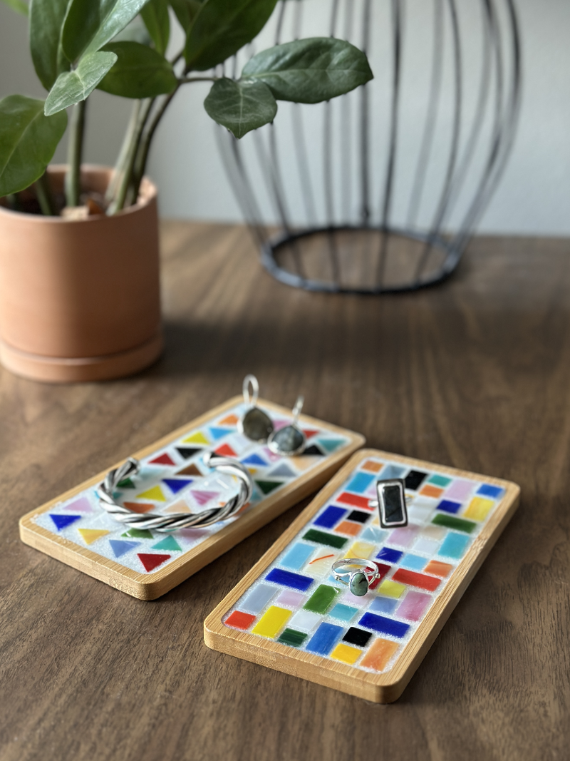 A photograph with colorful embroidery thread arranged in radiating lines around a building, next to green scissors, a pen, and an awl on a wooden surface.