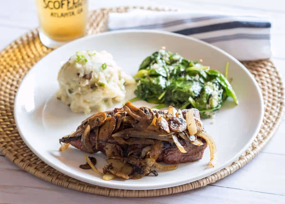 Steak topped with mushrooms with a side of mashed potatoes and greens.