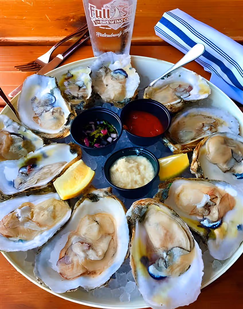 Oysters on the half shell in a bucket full of ice with dipping sauces.